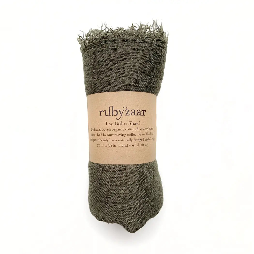 A rolled-up olive green shawl with fringed edges is positioned upright against a white background. The label reads "rubyzaar Boho Scarf," detailing it as a hand-dyed, bohemian-style accessory made from organic cotton in Thailand, measuring 72 x 29 inches, with instructions to hand wash and air dry.