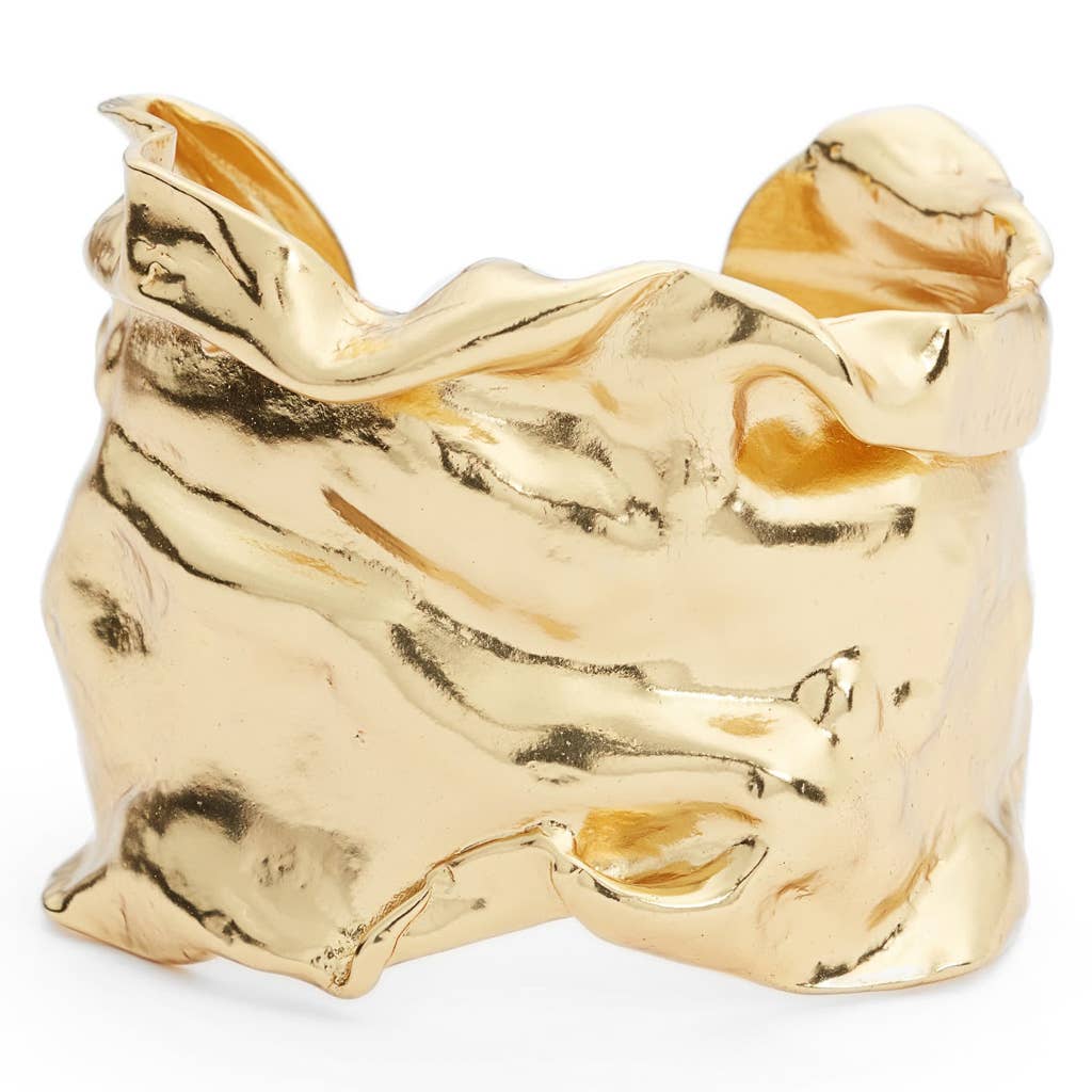The Crumpled Foil Cuff Bracelet boasts an organic, flowing design with a combination of smooth and textured surfaces that emulate natural forms. Its irregular edges and reflective gold plating give it a dynamic, sculptural look that captures varying light reflections. The adjustable cuff guarantees a perfect fit.