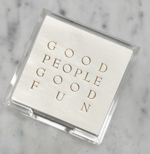 Load image into Gallery viewer, A stack of disposable napkins in a clear holder gracefully adorns a marble surface. The top napkin boasts gold embossed text stating &quot;GOOD PEOPLE GOOD FUN&quot; in crisp, uppercase letters. This chic Cocktail Napkin Acrylic Tray Set from the Year Round Entertaining collection makes an ideal hostess gift, guaranteed to impress guests with its charm and practicality.
