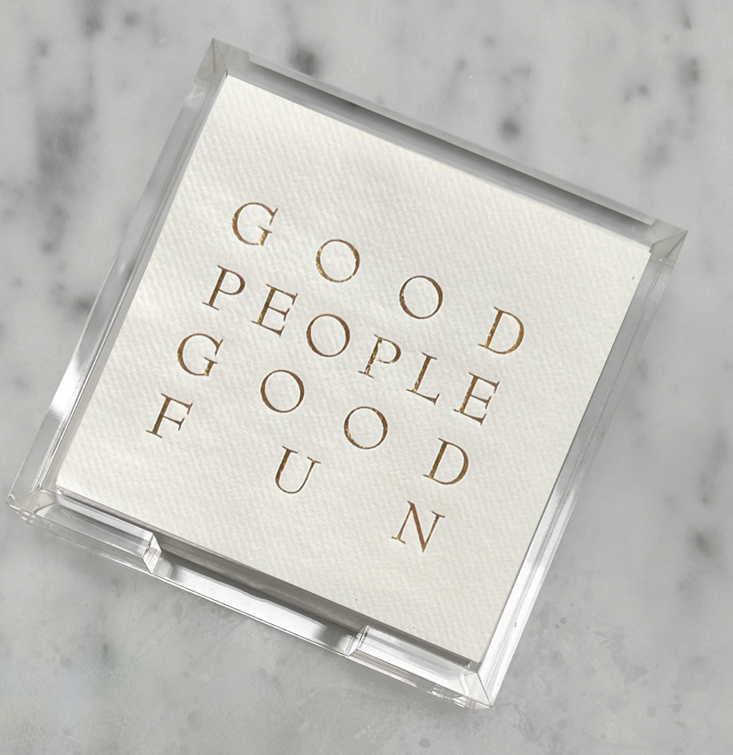 A stack of disposable napkins in a clear holder gracefully adorns a marble surface. The top napkin boasts gold embossed text stating 