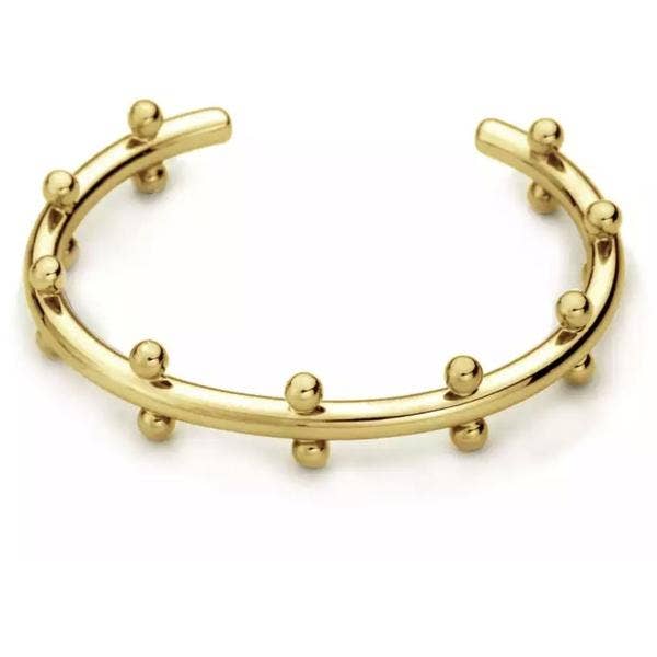 The Cindy Studded Cuff is an 18k gold-plated open cuff bracelet featuring evenly spaced small round studs along its edges. With a sleek, polished finish and a subtly curved design, this hypoallergenic and adjustable piece looks stunning against a plain white background.