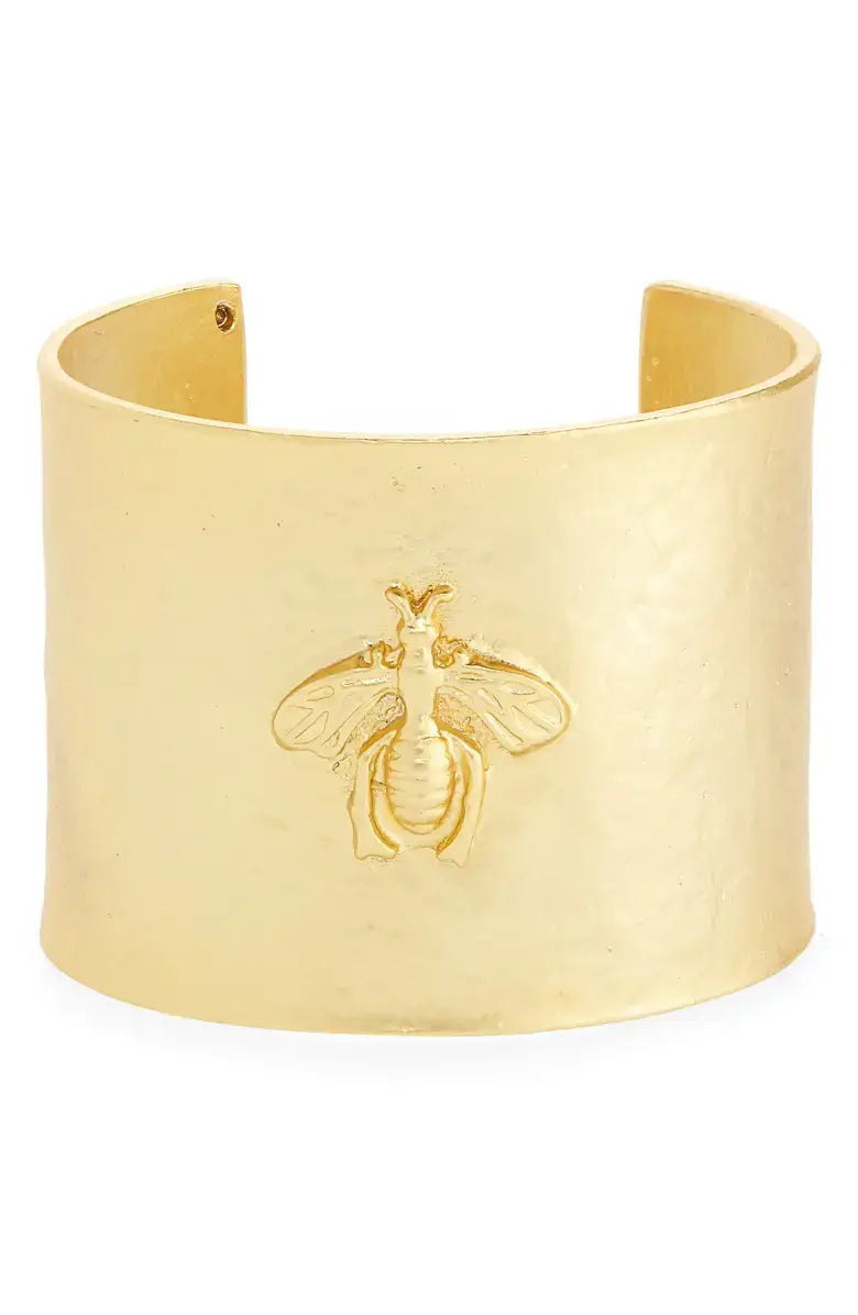 The Bee Design Hammered Cuff Bracelet is a wide gold bangle featuring a raised bee design at the center, with a smooth, hammered finish and an open back for adjustable fitting. The finely crafted bee detail adds an elegant touch to its minimalist design.