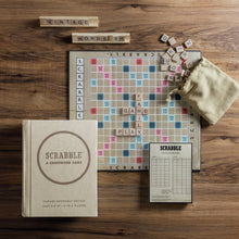 Load image into Gallery viewer, A Scrabble Vintage Bookshelf Edition board is laid out on a wooden table, with tiles forming the words &quot;FAME&quot; and &quot;PLAY.&quot; Nearby, more tiles are scattered from a small beige bag labeled &quot;VINTAGE WORDS.&quot; The Vintage Bookshelf Edition box, featuring premium game components, and a score sheet can also be seen.
