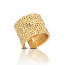 Load image into Gallery viewer, The Chainmail Ring is a wide piece with 24 kt gold plating and a textured, hammered surface that reflects light to create a shimmering effect. Slightly tilted on a smooth surface, it enhances its golden appearance and makes a bold statement.
