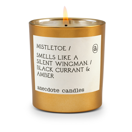 A gold tumbler candle with a flickering flame exudes holiday magic. The label reads 