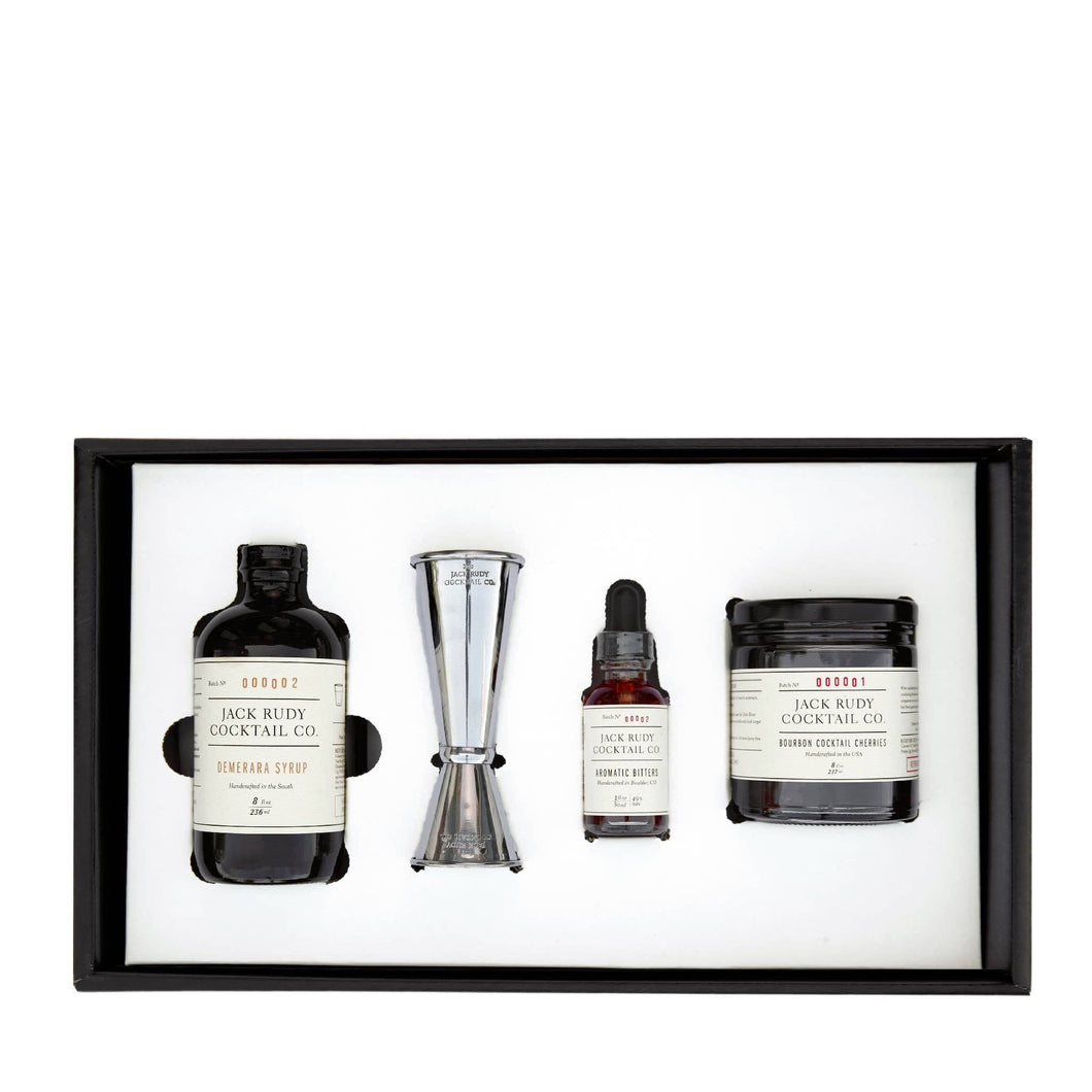 The Old Fashioned Kit - 4-pack, housed in a sleek black box, includes a bottle of syrup, a metal jigger, aromatic bitters, and cocktail cherries. Each item is labeled with the 