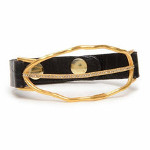 Load image into Gallery viewer, The Open Leaf W Crystal Line Leather Bracelet is crafted from black Italian leather, featuring an oval design with two uneven gold bands, one enhanced by Austrian crystals. A large round gold button offers a striking contrast to this elegant and sparkling textured piece.
