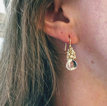 Load image into Gallery viewer, Close-up of a person wearing the White Topaz Clusters earring handcrafted at a San Francisco atelier. The earring features 14k gold-filled accents and a clear teardrop gem, elegantly dangling from the pierced ear and framed by long, light brown hair. The skin tone is light, with the image focusing on the ear area.
