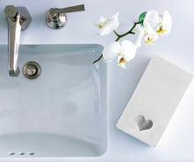 Load image into Gallery viewer, A top view of a white bathroom sink with a chrome faucet and soap dispenser. To the right, a white orchid with green stems lies next to Cloth-Like Guest Towels - Year Round Themes in a box adorned with a heart symbol. The scene is set on a pale surface for a clean and minimalist look.
.
