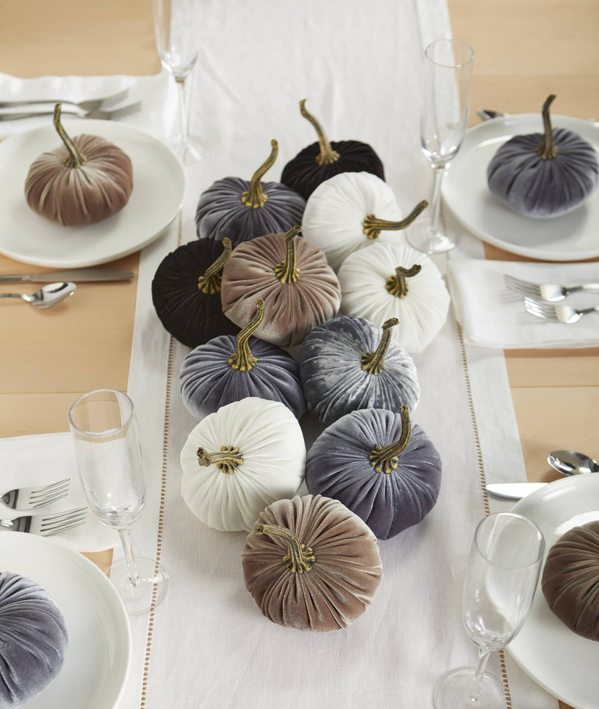 For an elegant autumn dining setup, a wedding centerpiece made from Handmade Small Velvet Pumpkins in vibrant colors like white, beige, gray, black, and purple is featured. The table arrangement includes a white runner complemented by place settings of pristine white plates and silver cutlery, creating the perfect fall decorating theme.