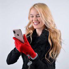 Load image into Gallery viewer, A smiling woman with long blonde hair wears a black fur coat and the Women&#39;s Stylish Touch Screen Gloves with Fur Trim &amp; Fleece in red, expertly combining tech-savvy practicality with fashion. She&#39;s intently looking at her smartphone against a plain, light grey background.
