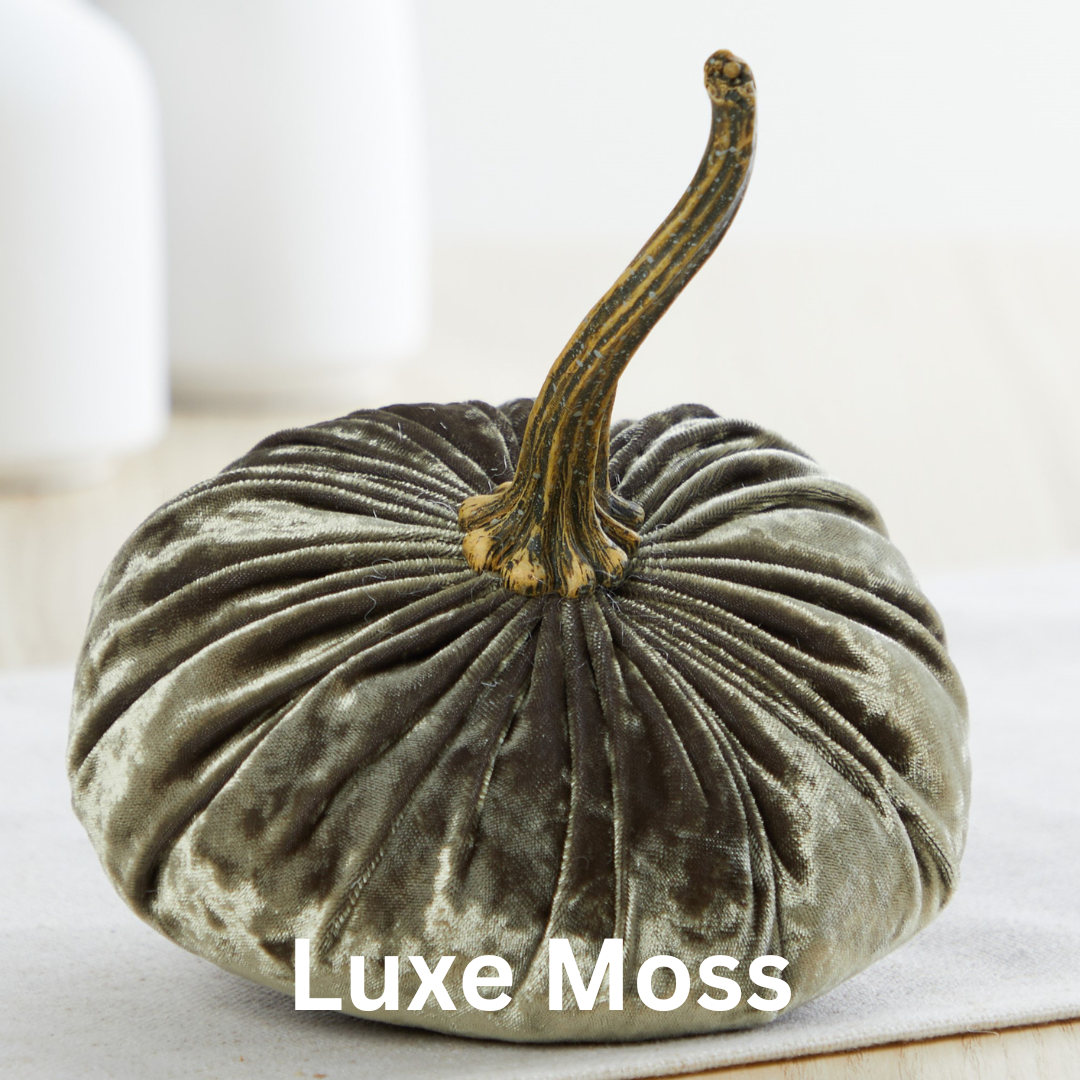 A handmade small velvet pumpkin crafted from luxurious, velvety moss-green fabric with a realistic brown stem, perfect for fall decorating. It's situated on a light-colored surface with a soft blur in the background. The text "Luxe Moss" is elegantly displayed in white at the bottom, making it an ideal choice for a wedding centerpiece.