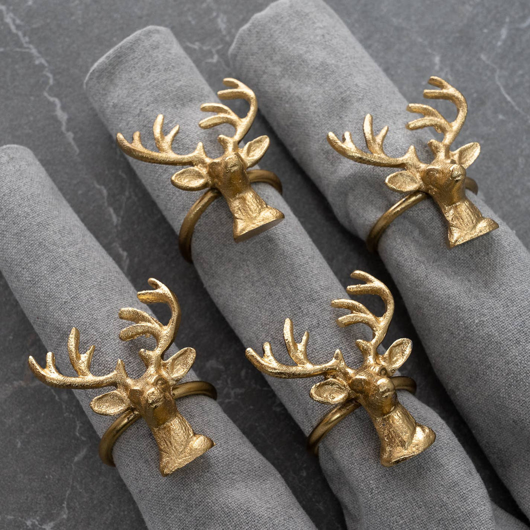 Gold Deer Napkin Rings from the set of 4 adorn rolled gray napkins, resting on a dark stone surface. These rings, crafted from sustainable materials with intricate antlers and detailed deer faces, add a rustic charm to the table setting.