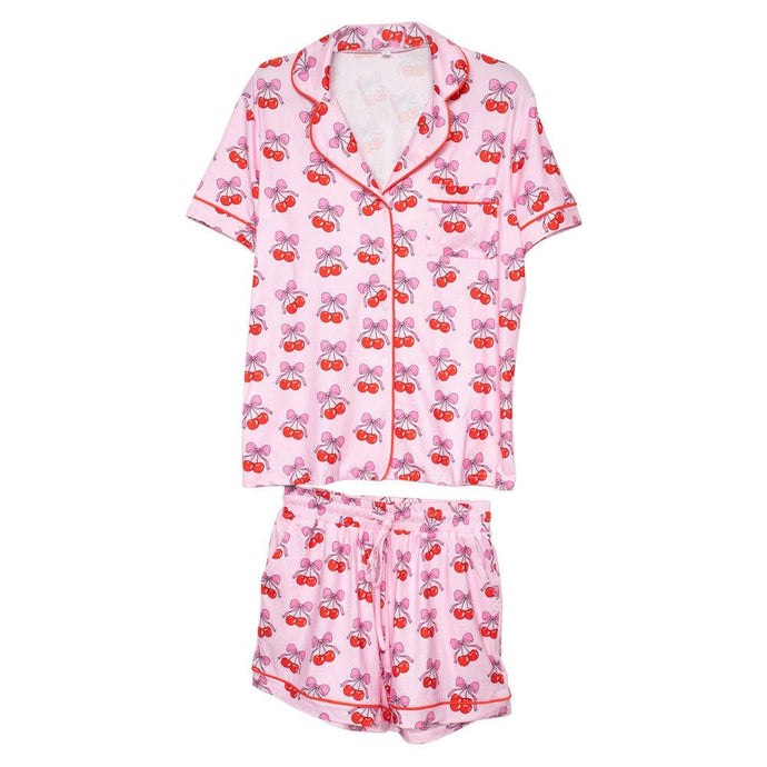 The Cherry Bow Cotton Pajamas set in pink includes short sleeves and shorts with a playful cherry bow print. Red piping on the collar, sleeves, and pockets offers a charming contrast, and the elastic waistband ensures comfort while lounging.