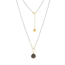 Load image into Gallery viewer, The Cassiopeia Necklace boasts two graceful gold-filled chains in a layered design. The shorter adjustable chain is adorned with a small drop pendant, while the longer chain features a rabbit-eared charm cradling a textured dark stone. Photographed against a white background, it beautifully accentuates its elegant gold-plated druzy accents.
