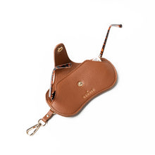 Load image into Gallery viewer, The Eclipse Eyewear Case is a brown vegan leather case with textured surface, a gold snap button, and &quot;FERAL&quot; embossed in gold. It includes a strap with a gold clip for easy attachment and holds tortoiseshell glasses, making it an ideal travel accessory.

