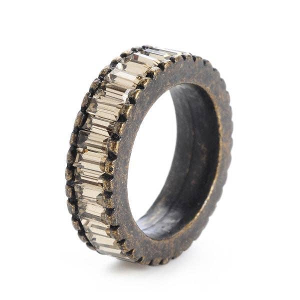 The Baguette Crystal Band Ring features a round, textured design with two rows of rectangular gemstones on a dark base, resembling black diamond crystals. It has a distressed antique brass finish for an aged look, and the smooth interior contrasts with the intricate crystal band design.