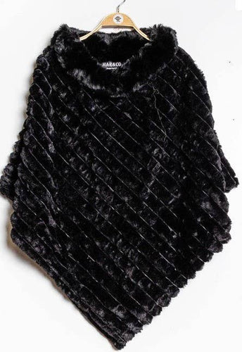 The Faux Fur Poncho, in black with a textured diagonal stripe pattern, provides cozy warmth. It is designed with a rounded neckline and is showcased on a wooden hanger against a white backdrop.