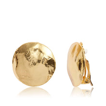 Load image into Gallery viewer, The image displays the Shell Disc Clip-On Earrings, featuring two round pieces with a hammered finish. The earring on the left showcases the lustrous, uneven front surface, while the one on the right reveals its side profile and clip-on mechanism. Each earring is 24-kt gold-plated, offering a distinctive artisanal appearance.
