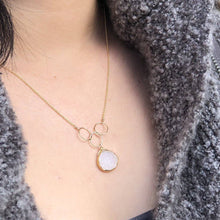 Load image into Gallery viewer, The Cassiopeia Necklace, featuring a gold-plated druzy pendant with three interlocking rings and a white stone, adorns the wearer&#39;s chest. The necklace, adjustable for comfort, elegantly complements their textured, dark gray sweater.
