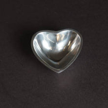 Load image into Gallery viewer, The Heart-shaped Bowl, made of shiny silver aluminum, features a metallic heart design centered against a black background. Its reflective surface creates bright spots and a glossy look that contrasts with the dark backdrop, enhancing its elegant simplicity.
