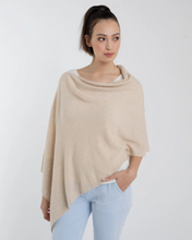 Load image into Gallery viewer, A person with long dark hair tied in a high ponytail is showcasing the Cashmere Poncho, styled over a white shirt and light blue jeans. They stand against a plain white background, gazing to the side with one hand in their pocket, exemplifying that this garment is truly one size fits all.
