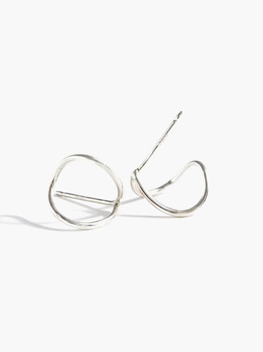 The Ear Hugs are minimalist sterling silver hoop earrings featuring a unique twisted design, set against a white background with a soft shadow. These open-ended earrings form an abstract circular shape and boast a smooth, polished finish that highlights the beauty of natural metal.