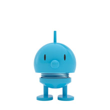 Load image into Gallery viewer, The Hoptimist Bumble is a small, round, blue toy figure with a smiling face and a spring body that captures the essence of Danish design history. It boasts a small nose, two black eyes, and a top fin, standing on two oval feet for a playful presence perfect for whimsical home decor.
