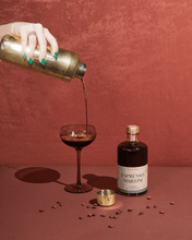 Load image into Gallery viewer, A hand adorned with green nail polish elegantly pours a dark cocktail from a gold shaker into a martini glass on the vibrant red surface. Next to it, the &quot;Espresso Martini Mixer&quot; bottle suggests a vodka infusion, while coffee beans and a gold cap enhance the textured, lively red backdrop.
