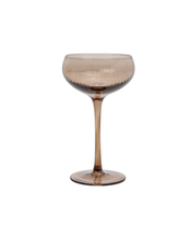 Load image into Gallery viewer, The Lou Coupe Glass, part of a set of two, features a sophisticated transparent smoky brown hue. Its elegant design incorporates a wide, shallow bowl atop a long, slender stem, enhanced by a subtle textured pattern that adds depth. The flat, round base ensures stability and grace when displaying craft cocktails. Perfect against a plain white background, this piece brings timeless charm to any setting.
