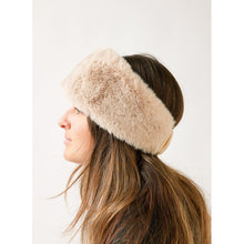 Load image into Gallery viewer, A person with long brown hair is seen in profile view, wearing the Cozy Cabin Headband, known for its cozy and fluffy beige design. The faux fur style covers the ears, indicating warmth. The plain and light background accentuates the texture of the headband and the person&#39;s straight hair cascading over their shoulders.
