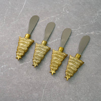 Load image into Gallery viewer, The Christmas Tree Spreaders - Set of 4 brings charm to any holiday gathering with their festive tree-shaped handles. The gold handles, featuring wavy ridges and star tips, beautifully complement the smooth matte gray stainless steel blades. When arranged diagonally on a textured gray surface, they create an elegant display.
