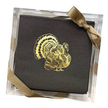 Load image into Gallery viewer, A stack of dark gray disposable napkins featuring a gold foil turkey design is neatly arranged in a clear, square holder from the &quot;Cocktail Napkin Acrylic Tray Set - Holiday Themed.&quot; A gold ribbon tied in a bow adorns the corner, adding an elegant touch ideal for holiday hosting.
