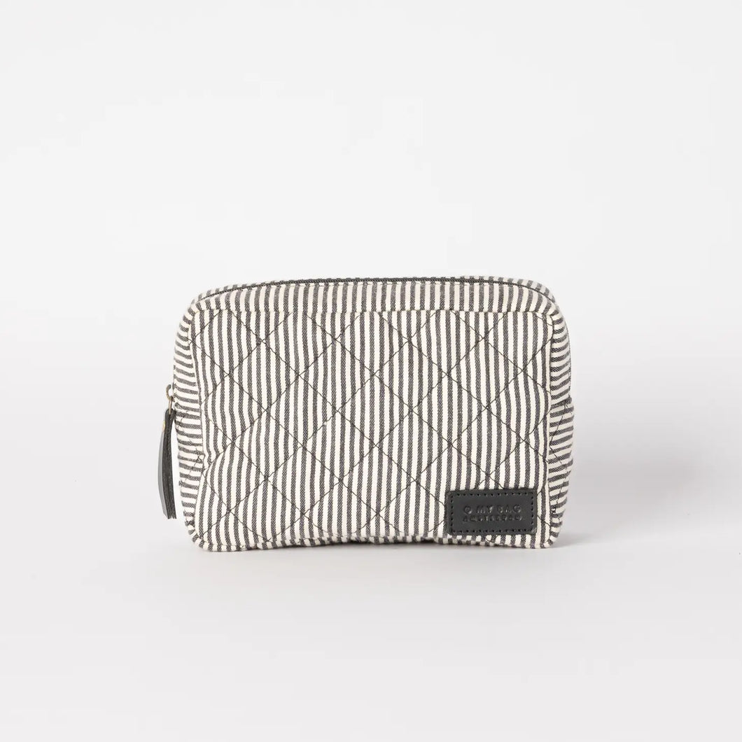 The Bella Pouch - Cotton/Black Classic Leather is a small, rectangular pouch flaunting a black and white striped pattern. Made from recycled cotton, it boasts a padded quilted design with diamond shapes. Positioned on a plain white background, its sustainable appeal is enhanced by a black label with stitching detail prominently displayed on the front lower right corner.