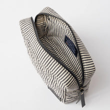 Load image into Gallery viewer, The Bella Pouch - Cotton/Black Classic Leather is open, displaying its roomy interior. Made from recycled cotton, the black and white striped design showcases a padded quilted pattern. Inside near the zipper, a small black tag is visible. The pouch sits against a simple white backdrop.
