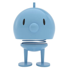 Load image into Gallery viewer, The Hoptimist Bumble embodies the charm of Danish design history with its blue, round, cartoonish figure featuring a large head, small black oval eyes, and a small cylindrical nose. Its spring neck and simple legs make it not only playful but also a delightful piece of home decor inspired by the classic Hoptimist.
