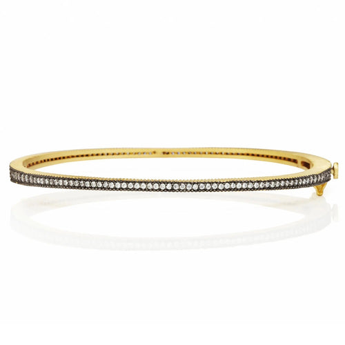 The Classic Pavé Hinge Bangle is a slender gold accessory adorned with a row of dazzling diamonds. Placed on a white backdrop, it boasts a smooth finish that gently reflects light, accentuating its sophisticated design.