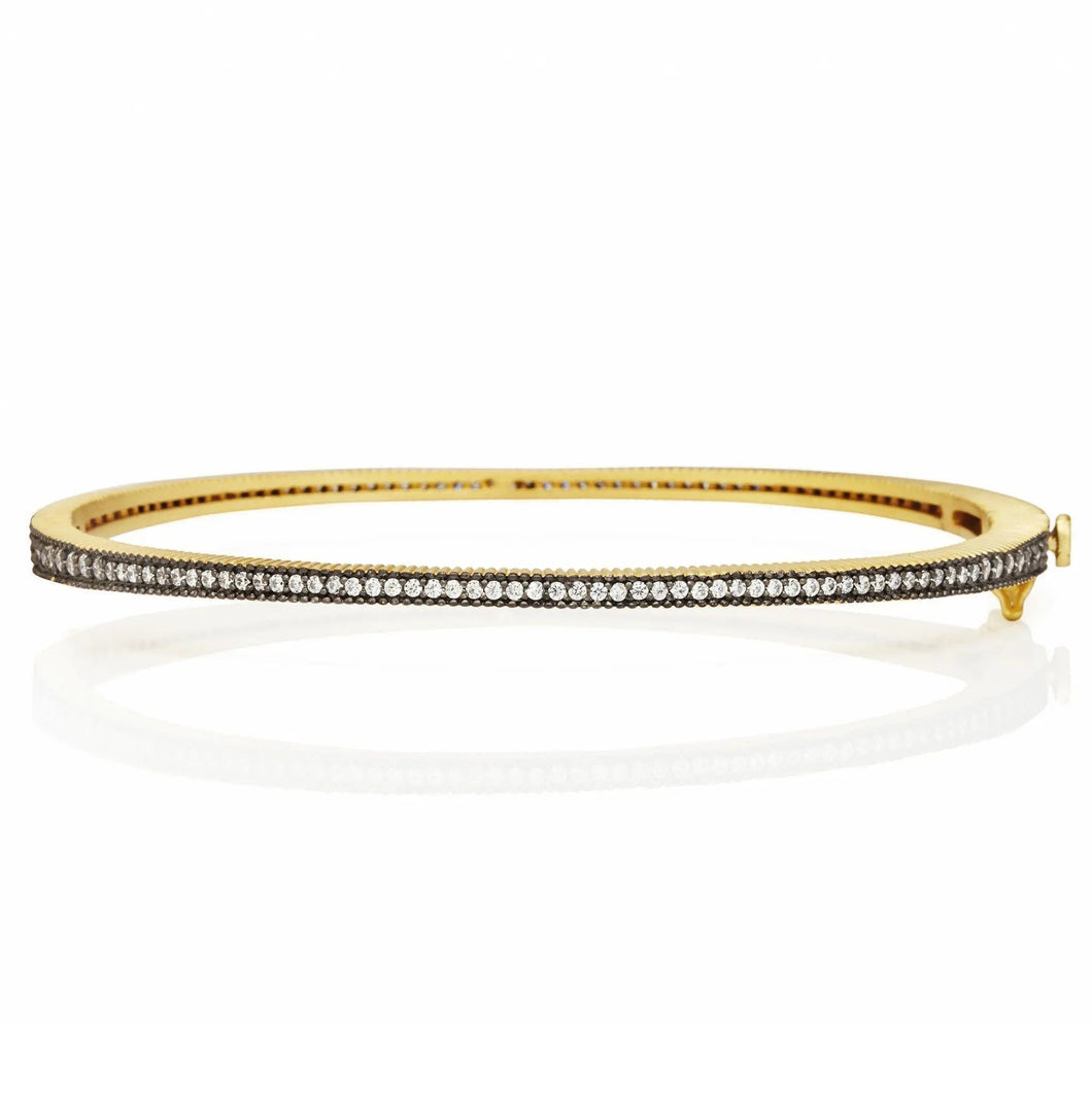 The Classic Pavé Hinge Bangle is a slender gold accessory adorned with a row of dazzling diamonds. Placed on a white backdrop, it boasts a smooth finish that gently reflects light, accentuating its sophisticated design.