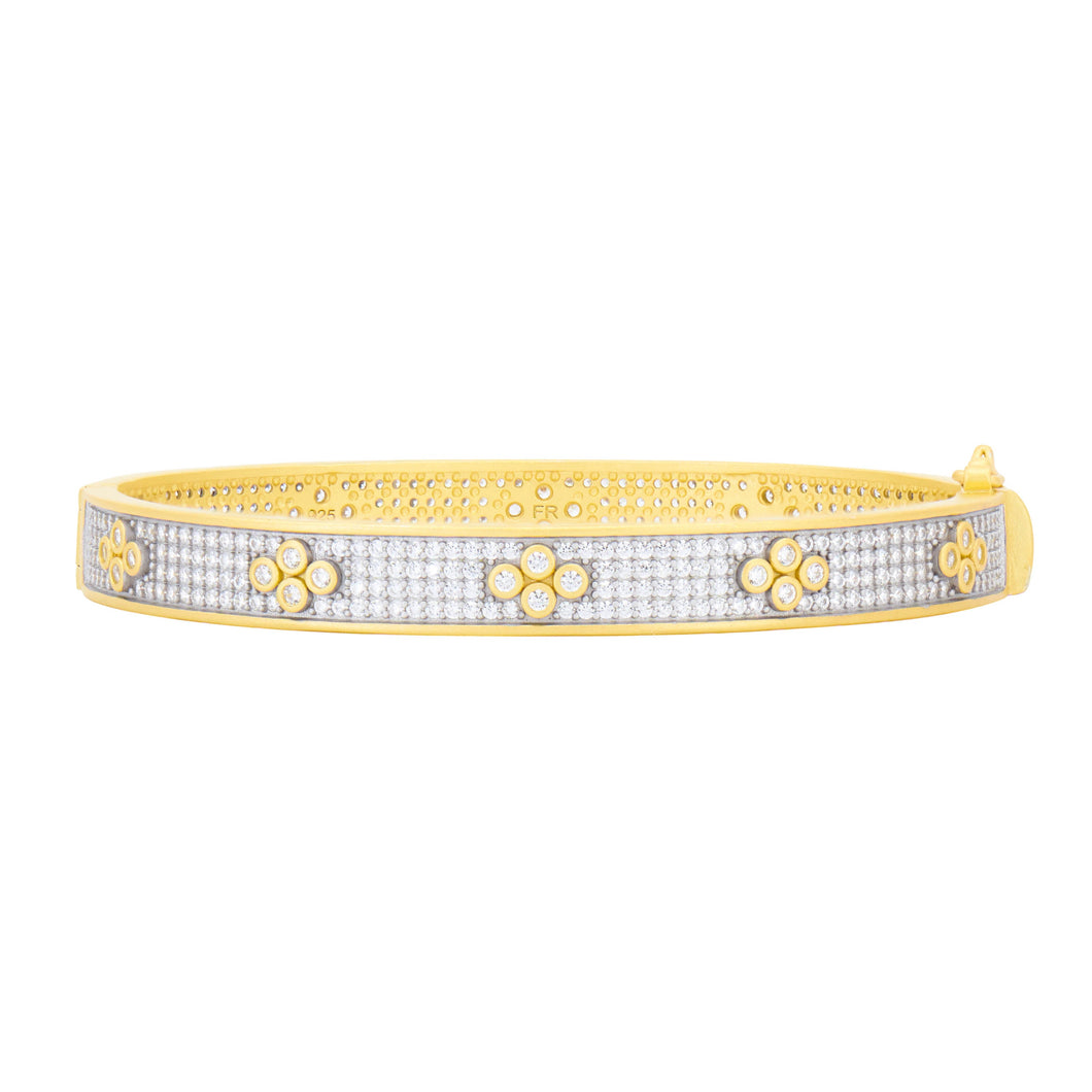 Introducing the Signature Brooklyn in Bloom Clover Hinge Pave Bangle: a dazzling piece crafted with sterling silver and gold. The outer band showcases clusters of small round diamonds reminiscent of blooming flowers, enhanced by black rhodium accents. Inside, intricate engravings grace the gold surface, highlighted by a visible clasp.