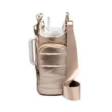 Load image into Gallery viewer, The HydroBag Handle is a gold insulated drink holder with a shiny finish, complete with an elastic straw holder and a front zippered pocket. This stylish piece includes an adjustable shoulder strap and securely holds a large tumbler with a white lid behind the main compartment. Its quilted design enhances its fashionable appeal.
