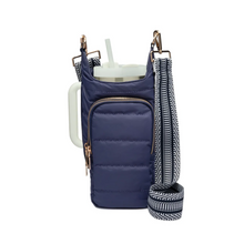 Load image into Gallery viewer, The HydroBag Handle, crafted from dark blue quilted fabric, features a front zippered pocket that elegantly cradles a white tumbler with an elastic straw holder. Beside it hangs a detachable strap in a black and white chevron pattern. The structured design and gold-tone hardware enhance its charm.
