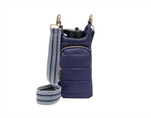 Load image into Gallery viewer, The HydroBag, in a quilted navy blue finish, showcases gold zippers and a front pocket. Its detachable strap features a navy and white chevron pattern, while its design as an ORIGINAL puffer water bottle bag is accentuated by the reusable water bottle that stands out against the plain white background.
