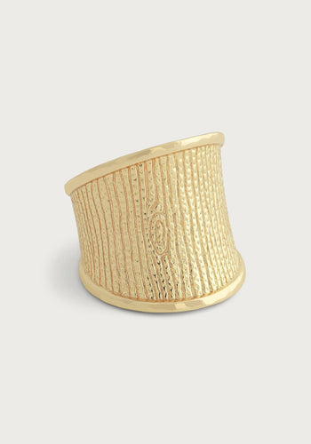 Introducing the Enchanted Forest Bark Ring, an exquisite gold ring showcasing a textured woodgrain motif that mimics tree bark. It features vertical lines and an oval knot design on a micro-hammered 18k gold band. The ring is wide at the front but elegantly tapers towards the bottom, offering a modern and unique look against a plain, light gray background.