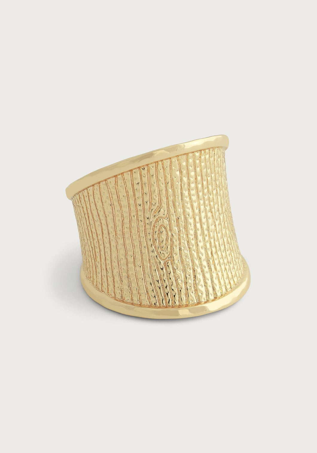 Introducing the Enchanted Forest Bark Ring, an exquisite gold ring showcasing a textured woodgrain motif that mimics tree bark. It features vertical lines and an oval knot design on a micro-hammered 18k gold band. The ring is wide at the front but elegantly tapers towards the bottom, offering a modern and unique look against a plain, light gray background.