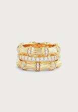 Load image into Gallery viewer, Introducing the Bamboo Stack Ring: an 18k gold piece featuring a bamboo-inspired design with two intertwined bands. These bands are gracefully embellished with pavé crystals that shimmer delicately across the top half, set against a simple, light gray backdrop.
