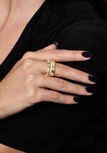 Load image into Gallery viewer, A hand with long, dark-painted nails is adorned with the Bamboo Stack Ring in 18k gold, featuring intricate designs and pavé crystals. The wearer is dressed in a black garment, providing a contrasting backdrop that accentuates the elegance of the jewelry.
