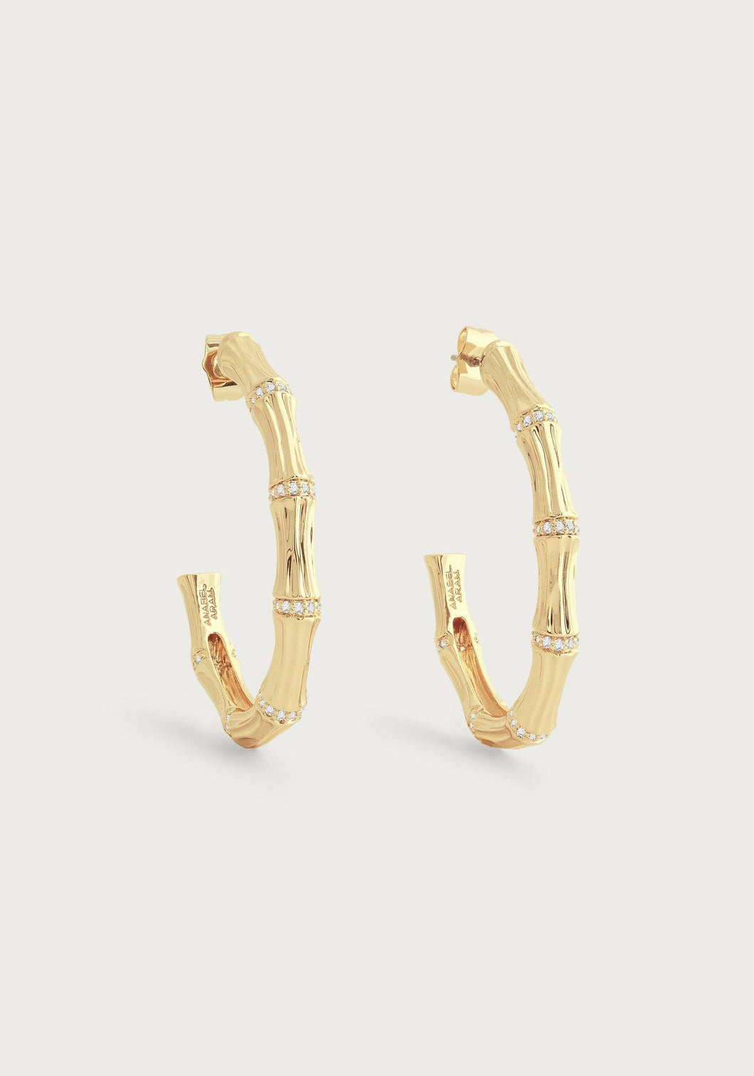 The Bamboo Single Hoop Earrings showcase a bamboo-inspired design with alternating textures made from 18k gold-dipped brass. These hoops are adorned with small, sparkling crystals arranged in a straight line along the bamboo sections, set against a plain, light backdrop to highlight their shine and intricate detail.