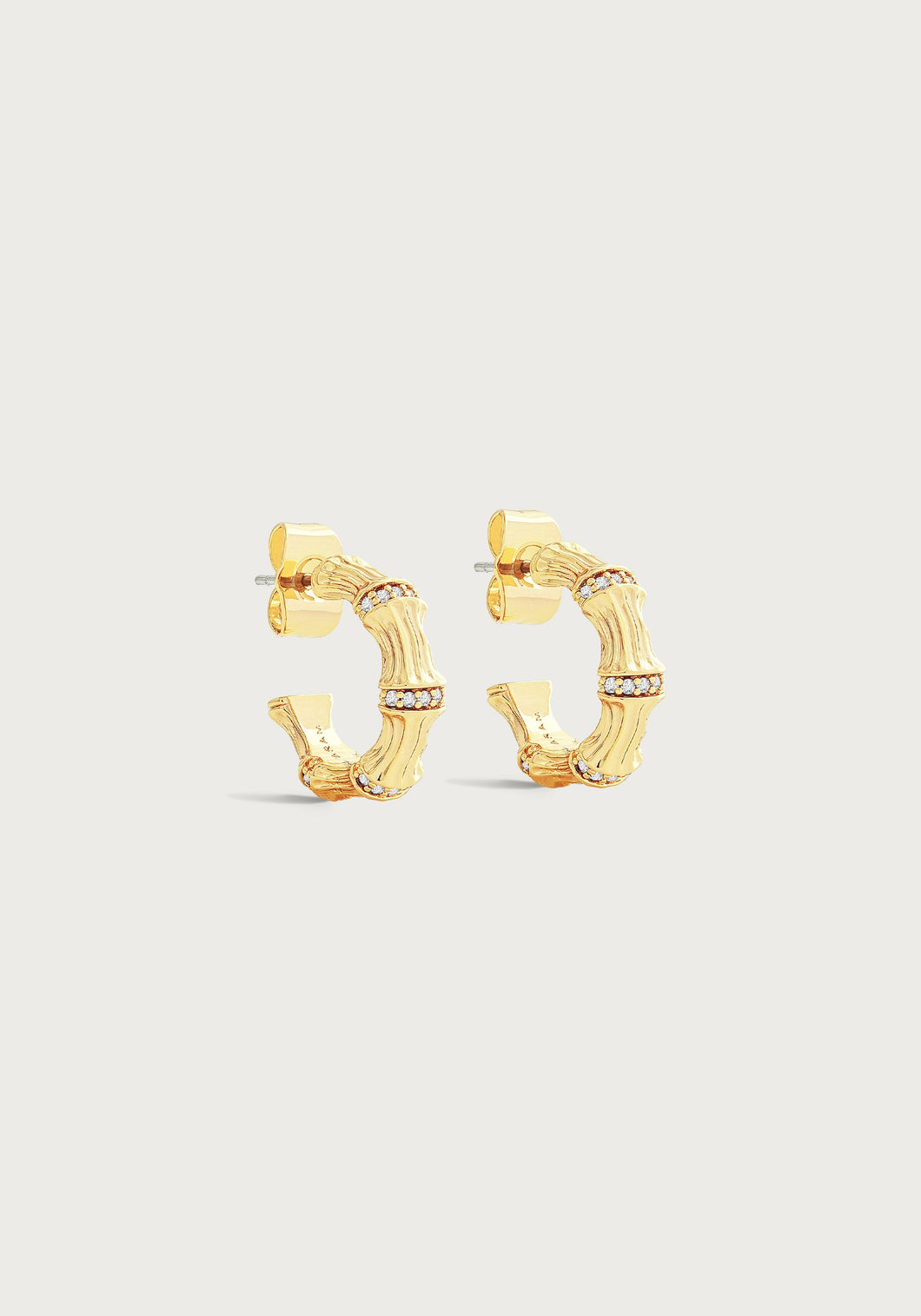 The Bamboo Huggie Hoop Earrings exude a chic style with their textured bamboo-inspired design and delicate sparkling stones adorning the edges. Made from gold-plated brass, these earrings boast a shiny finish, beautifully contrasted against a plain, off-white background.