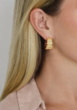 Load image into Gallery viewer, A close-up reveals a person with long blonde hair wearing the Enchanted Forest Bark Hoops, elegant textured earrings dipped in 18k gold. The lustrous, wide statement piece exudes sophistication, beautifully complementing their light pink collared shirt against a neutral background that highlights the earring&#39;s woodgrain motif.
