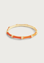 Load image into Gallery viewer, The Bamboo Enameled Hinge Bangle is a beautifully crafted piece designed to resemble bamboo, featuring segments of vibrant orange inlay. The smooth and polished surface includes engraved details that enhance the bamboo effect. Made of 18k gold-dipped brass, the inside features an inscribed message against a plain off-white background.
